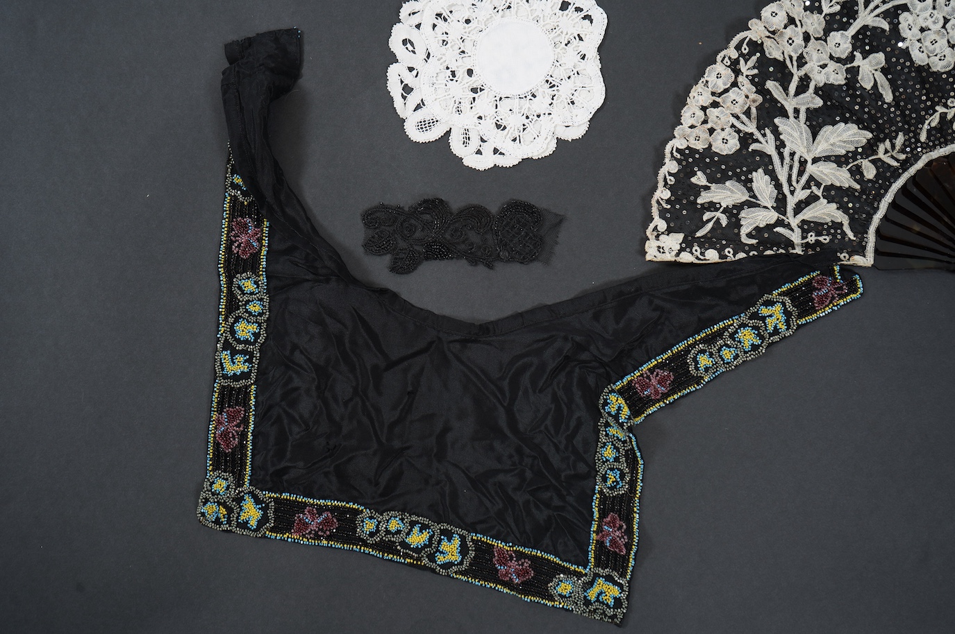 A French tortoiseshell, net, sequin and Honiton bobbin lace fan, with a collection of Jet appliques, a bead work fronter, embroidered mats and silk mats, an early Tiffany &Co poshette and embroidered appliqués and a Le M